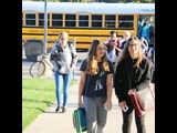 Kids walking to school from a school bus in the background.