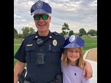 Police officer and a young girl posing with their police hats on at a park.